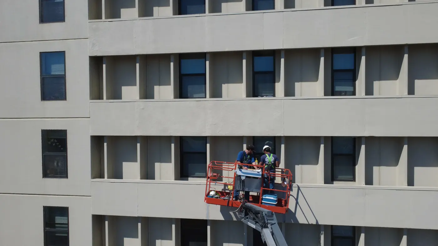 Dos miembros del equipo de Midwest con cascos y arneses trabajando desde la canasta de una grúa elevadora