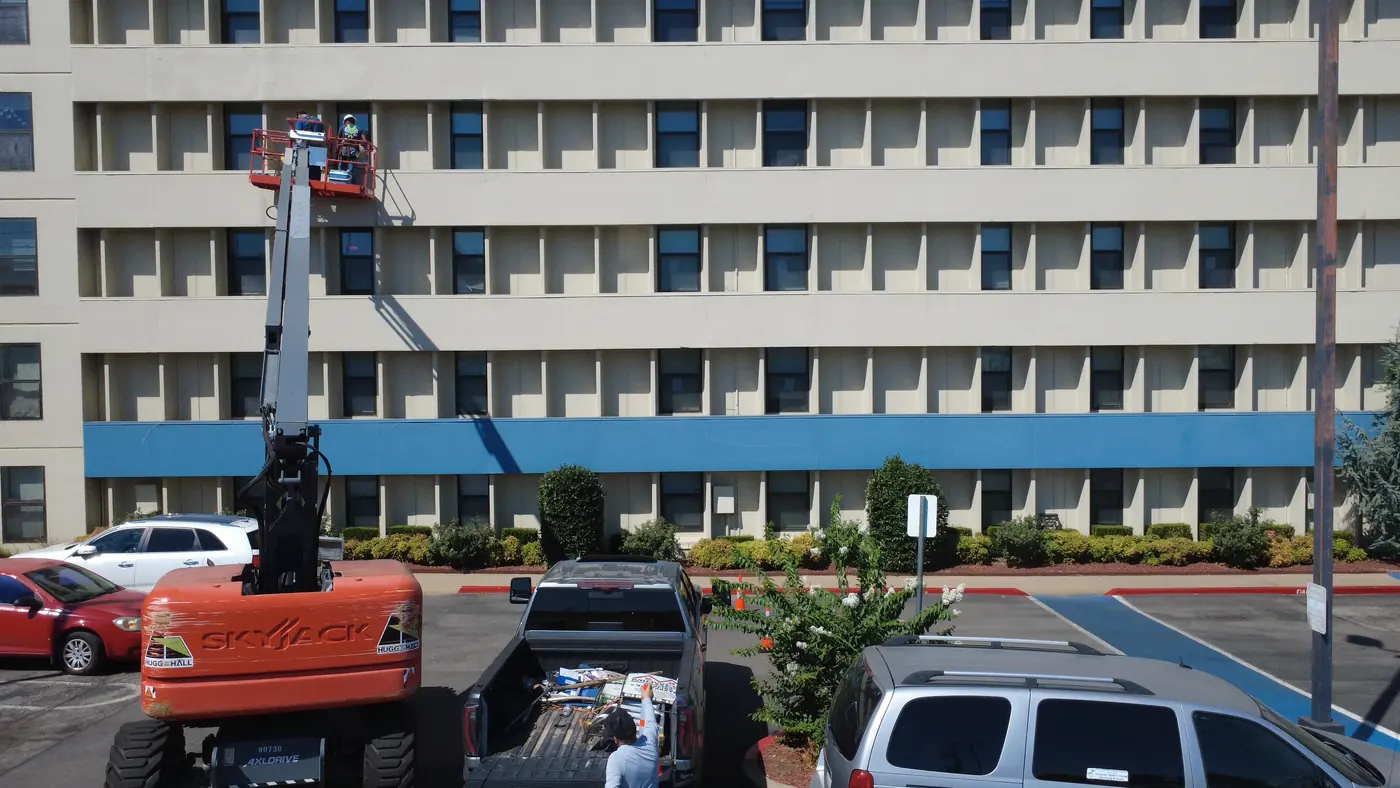 Una grúa elevadora extendida contra un edificio comercial de siete pisos con equipos trabajando la fachada