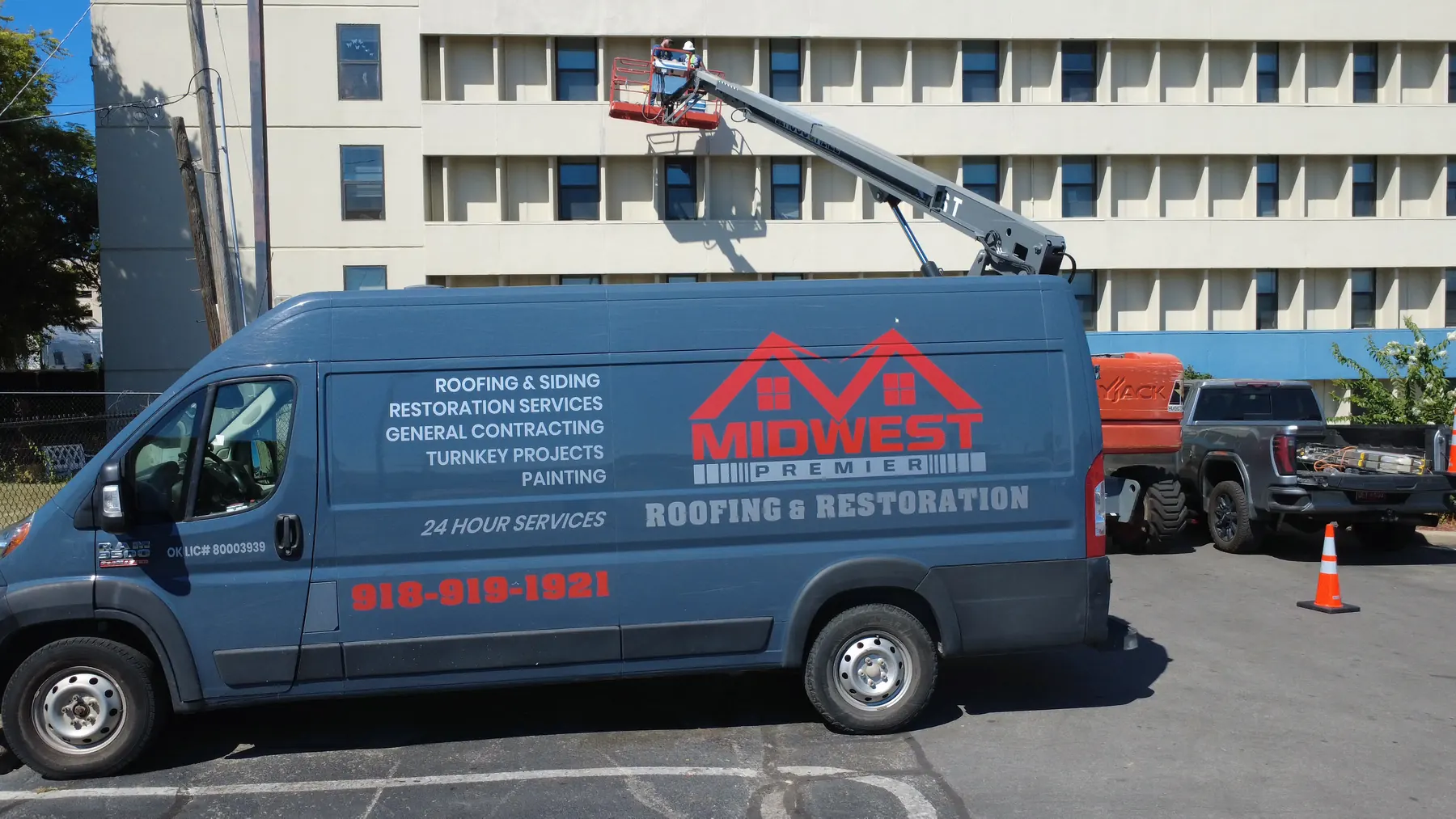 Una camioneta de Midwest Premier Roofing en una obra comercial en Tulsa, con equipos trabajando la fachada desde una grúa elevadora