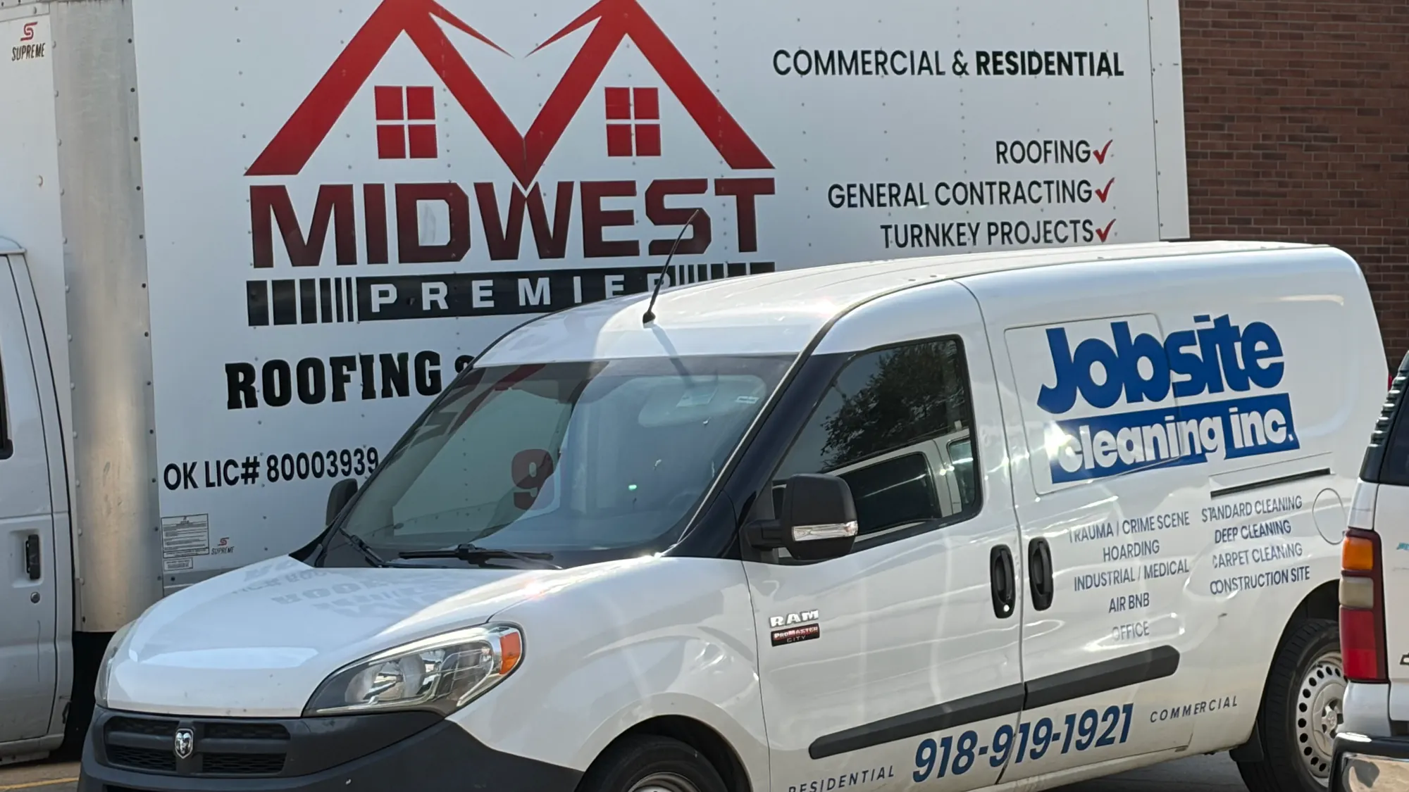 A Midwest Premier Roofing box truck and a Jobsite Cleaning Inc. van parked together outside the Tulsa yard